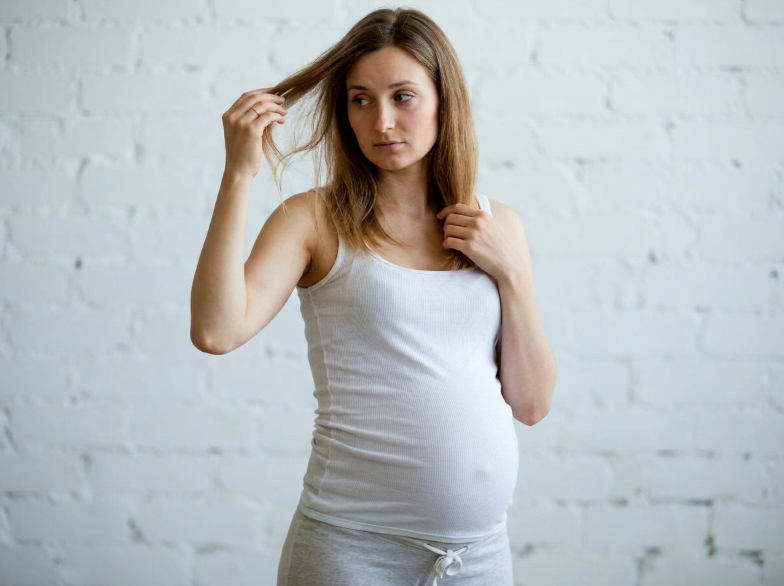 Pregnant woman gently examining her hair, reflecting on hair changes during pregnancy — SIMONE TRICHOLOGY