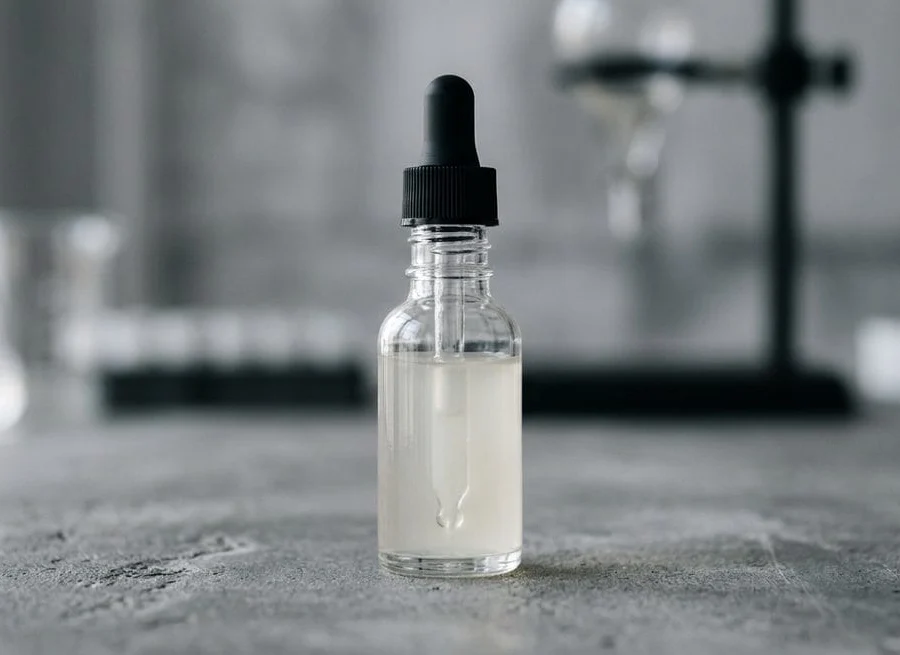 Glass dropper with a drop of hair serum on a grey laboratory background — trichoceuticals vs dermocosmetics