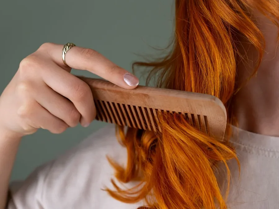 Woman combing the ends of her long, curly red hair with a wooden comb