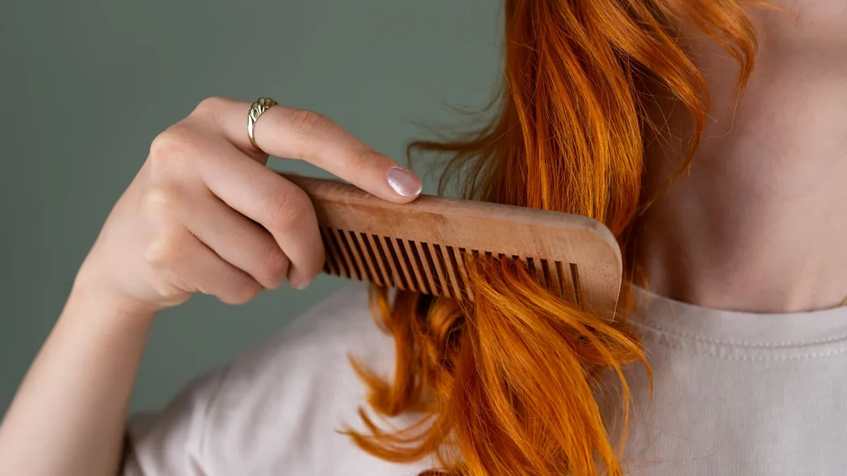 Woman combing the ends of her long, curly red hair with a wooden comb