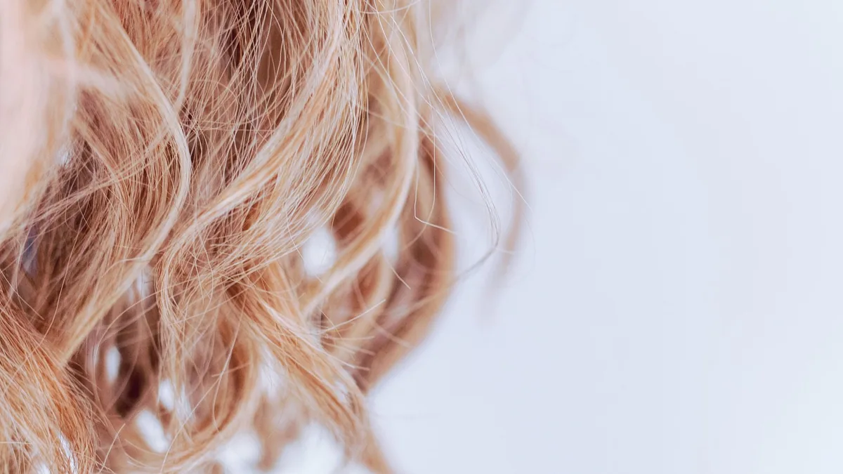 Gros plan de mèches de cheveux blond clair ondulées sur fond blanc, illustrant la composition du cheveu