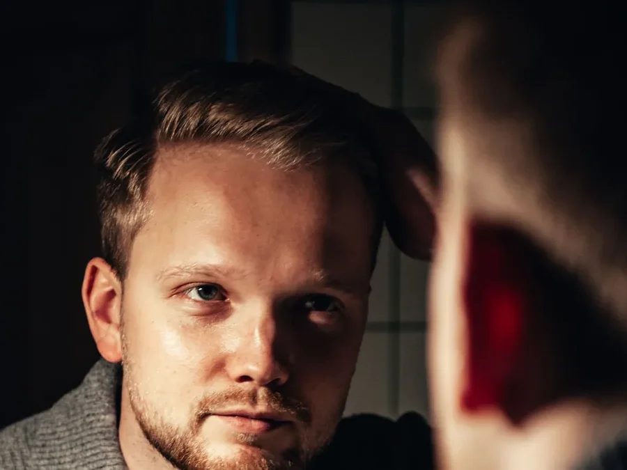 Man fixing his hair in front of a mirror while checking his hairline for signs of male pattern hair loss