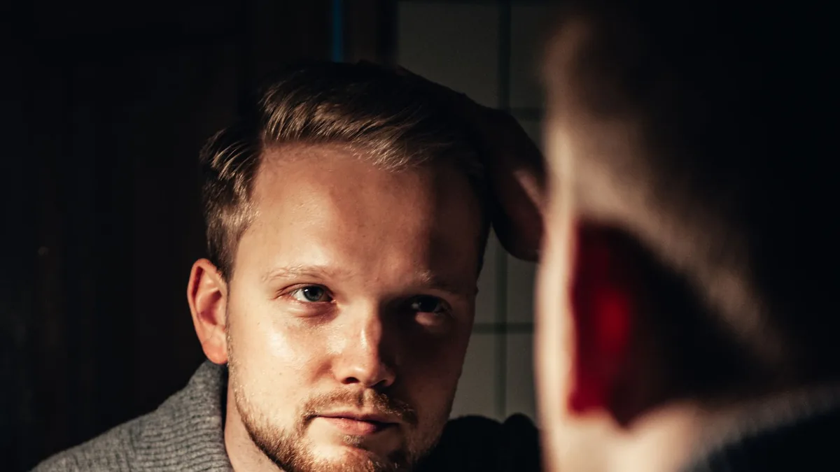Man fixing his hair in front of a mirror while checking his hairline for signs of male pattern hair loss