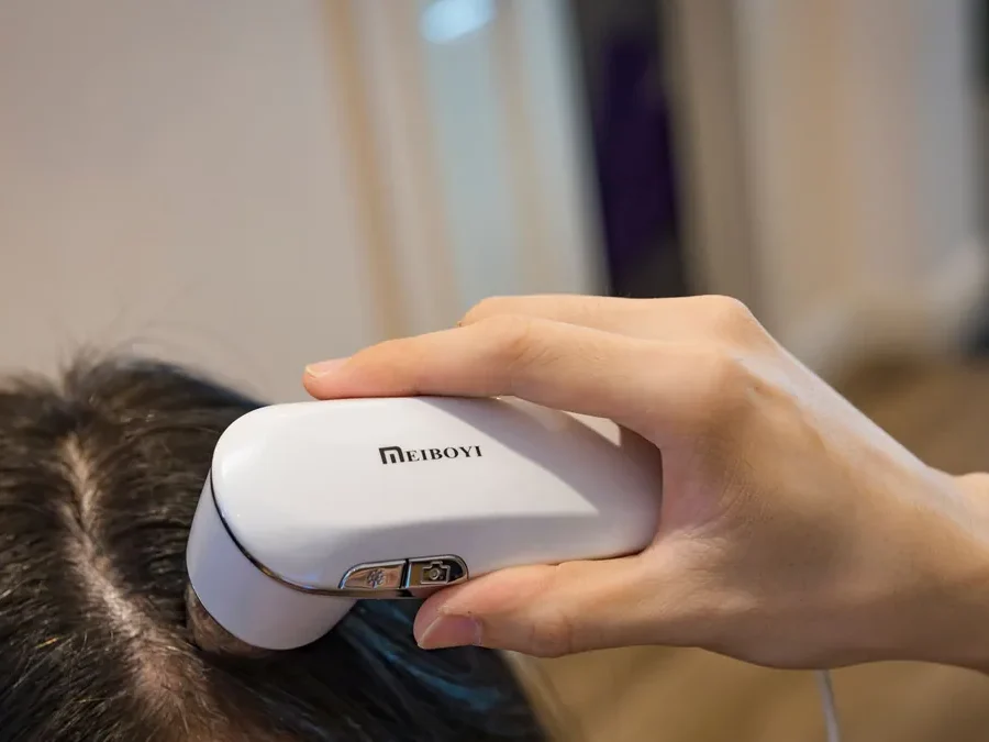 Woman holding a small handheld trichoscope used to examine the scalp and hair before a hair analysis appointment