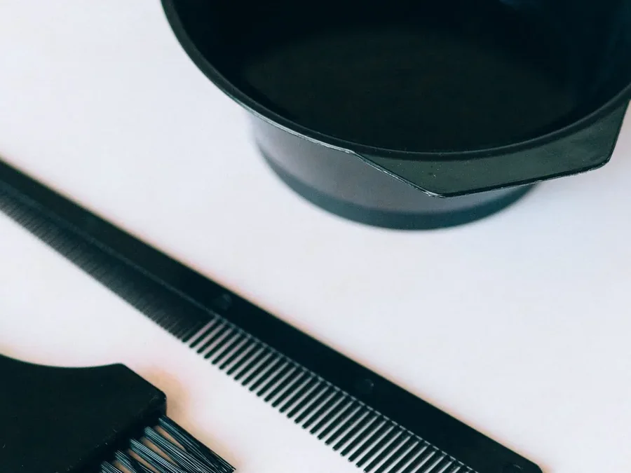 Black mixing bowl, application brush and comb on a white surface: the basic tools used to mix and apply hair dye