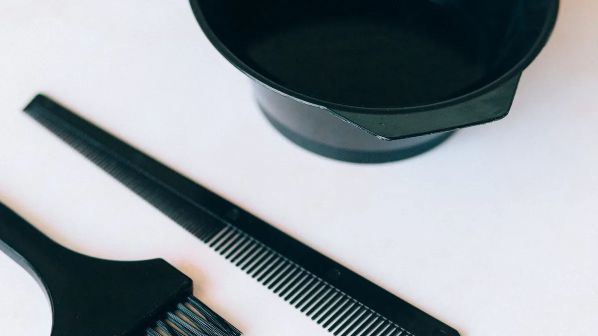 Black mixing bowl, application brush and comb on a white surface: the basic tools used to mix and apply hair dye