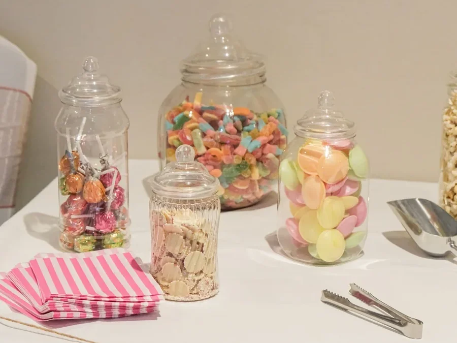 Jars of colorful candy, sweets and popcorn on a table – sugary snacks and hair health