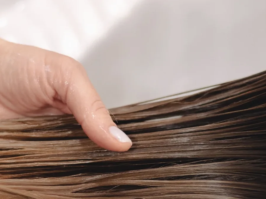 Hand holding long, wet brown hair over a white sink during a hair wash
