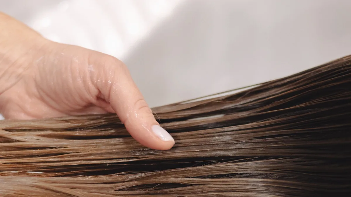 Hand holding long, wet brown hair over a white sink during a hair wash