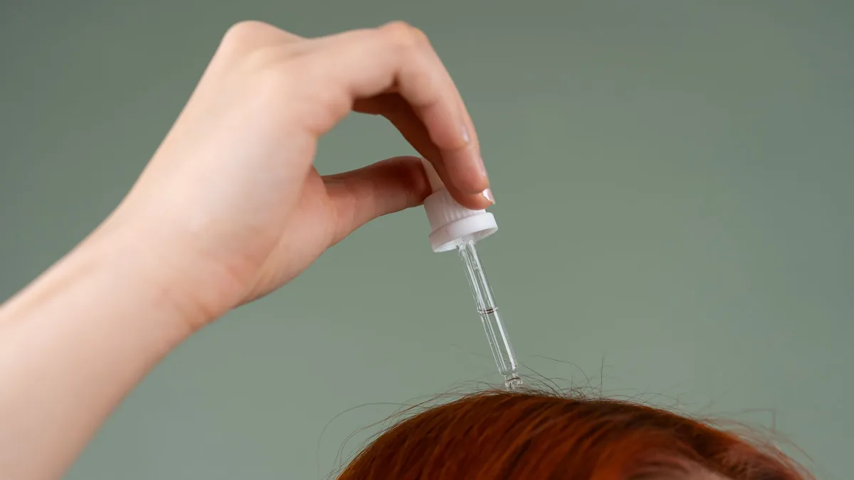 Hand mit Glaspipette trägt ein Kopfhautserum auf rotes Haar auf – Pflege als Ergänzung zur Sauerstoffbehandlung