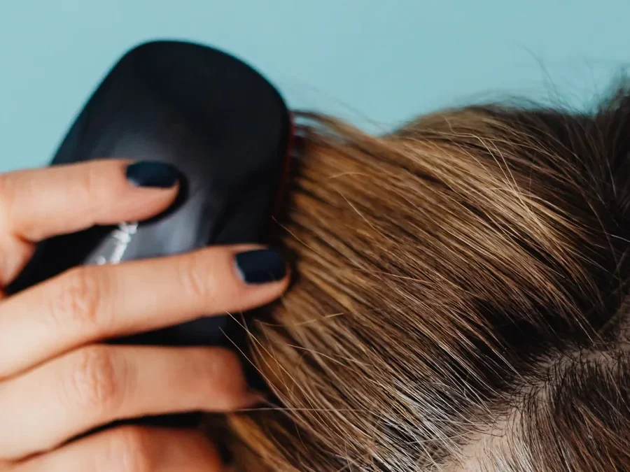 Close-up of a woman gently brushing her roots along her part with a scalp brush