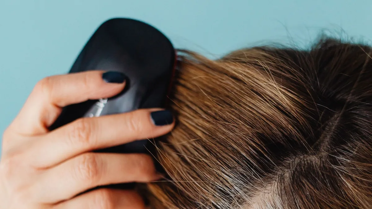 Close-up of a woman gently brushing her roots along her part with a scalp brush