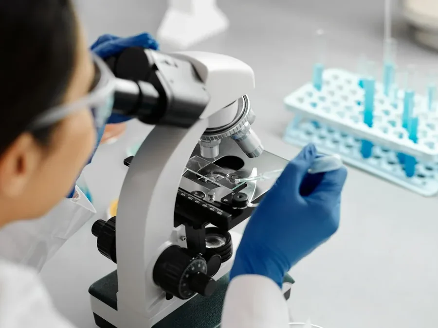 Researcher in blue gloves looking through a microscope in a lab, as in a hair shaft examination