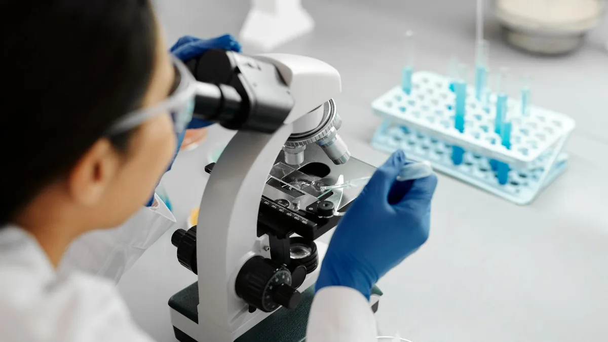 Researcher in blue gloves looking through a microscope in a lab, as in a hair shaft examination